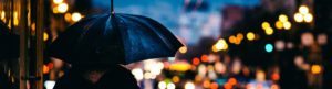 image of a person holding an umbrella on a rainy city street corner for Pennsylvania Umbrella Insurance